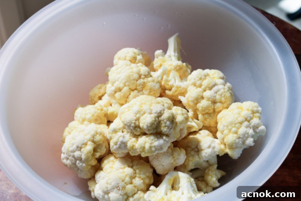 Cauliflower florets being tossed with olive oil in a bowl