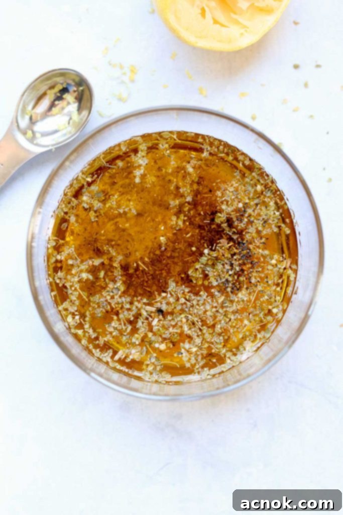 Freshly prepared oregano vinaigrette in a white bowl with whisk, showing its smooth texture