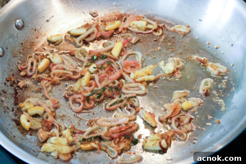 Cooked shallots in a pan, with thyme stems and lemon pieces optionally removed.