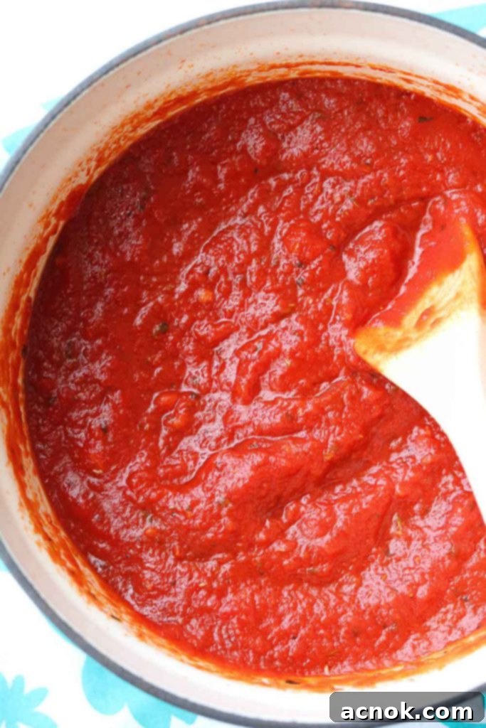 Rich and Zesty homemade pizza sauce simmering gently in a small saucepan, ready to be spread on pizza dough.