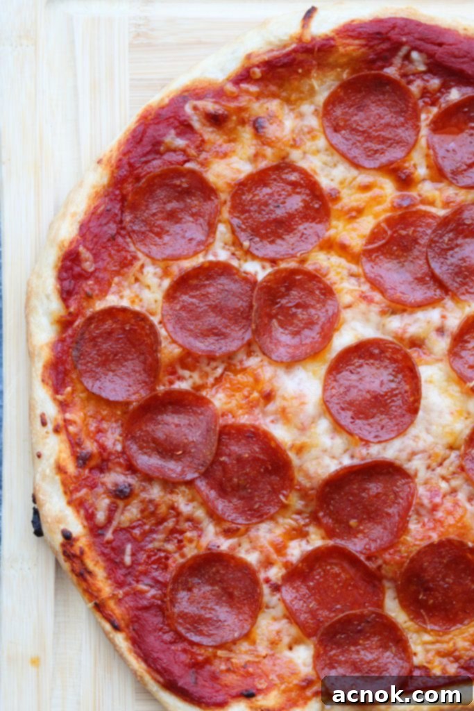 A freshly baked homemade pepperoni pizza, generously topped with Rich and Zesty Pizza Sauce, resting on a wooden chopping block.