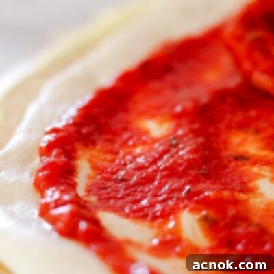 A close-up of the vibrant Rich and Zesty Pizza Sauce spread on fresh pizza dough, ready for toppings.