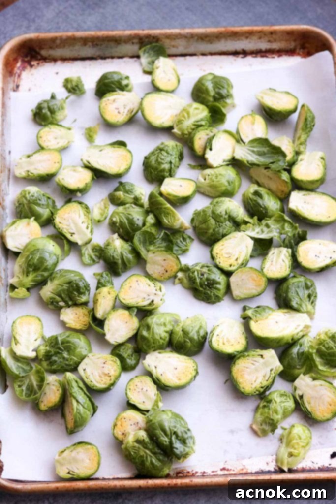 Brussels sprouts halves tossed with olive oil, salt, and pepper on a baking sheet, ready for roasting.