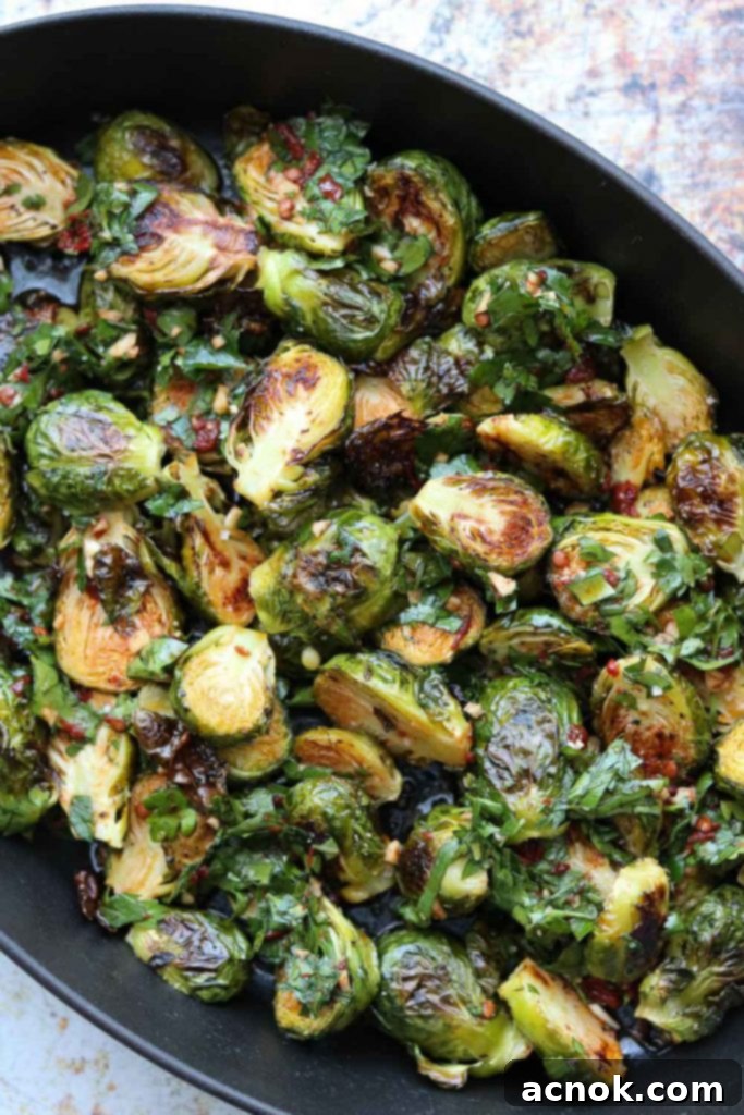 Roasted Brussels sprouts generously topped with red chimichurri, served in a cast iron pan.