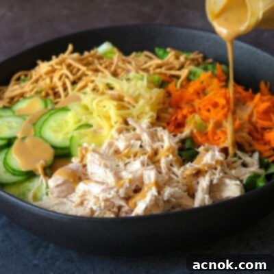 chinese chicken salad ingredients in black bowl with salad dressing being poured onto