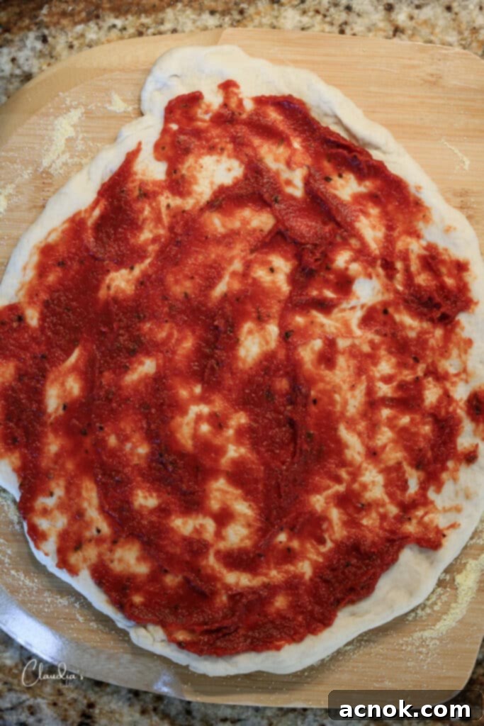 adding pizza sauce and toppings to a pizza on the peel