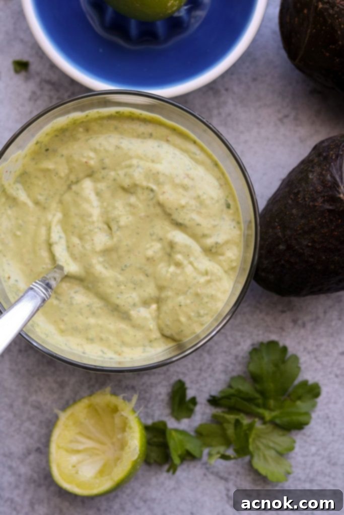 Creamy avocado dressing in a clear bowl, garnished with lime wedges and fresh parsley, ready to serve.