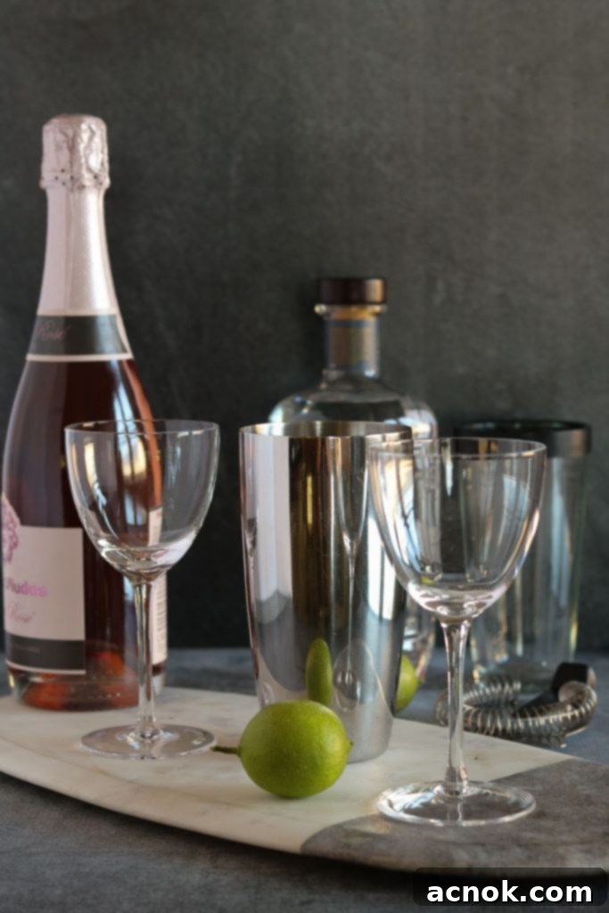 Raspberry Tequila Fizz 3 Ingredients laid out for a Sparkling Raspberry Tequila Cocktail: sparkling rosé, fresh raspberries, lime, silver tequila, and simple syrup, alongside a cocktail shaker and coupe glasses.