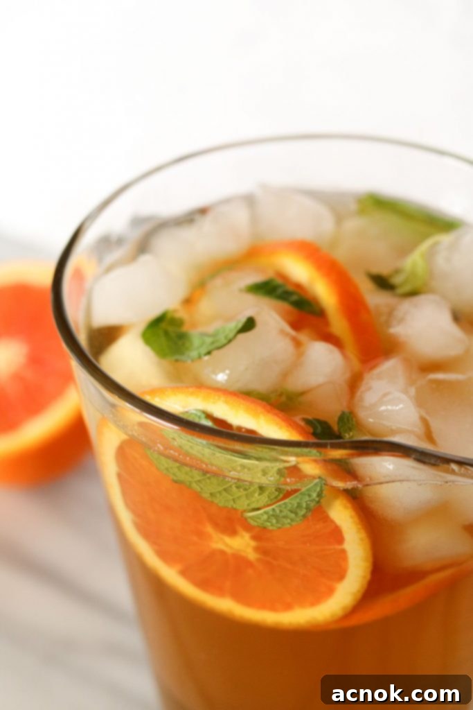 Vibrant iced green tea with orange and mint, garnished with fresh slices and leaves in a glass.