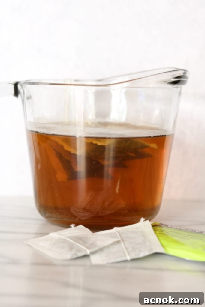 Close-up of green tea bags steeping in hot water within a clear glass container, with steam gently rising.