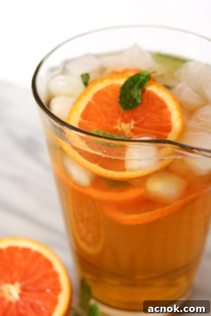 Slices of fresh orange being added to the pitcher of green tea, mint, and ice, completing the visual appeal.