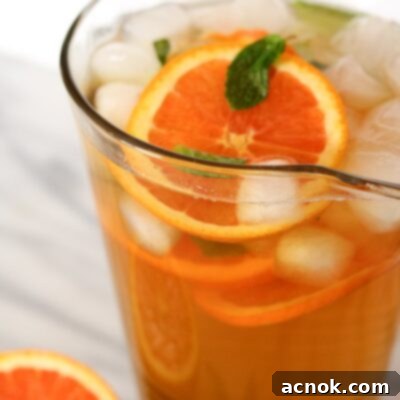 Final step of making honey orange mint green tea, poured into a glass with garnishes.