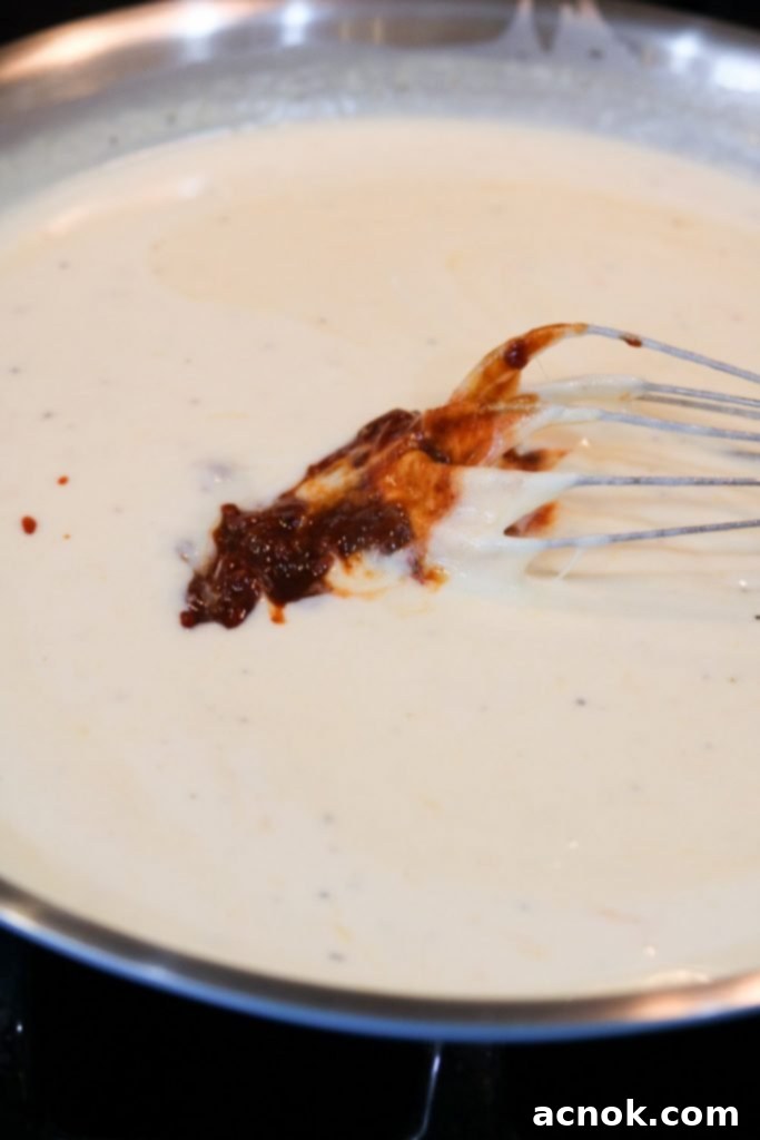 Minced chipotle peppers in adobo being added to the rich cheese sauce for flavor