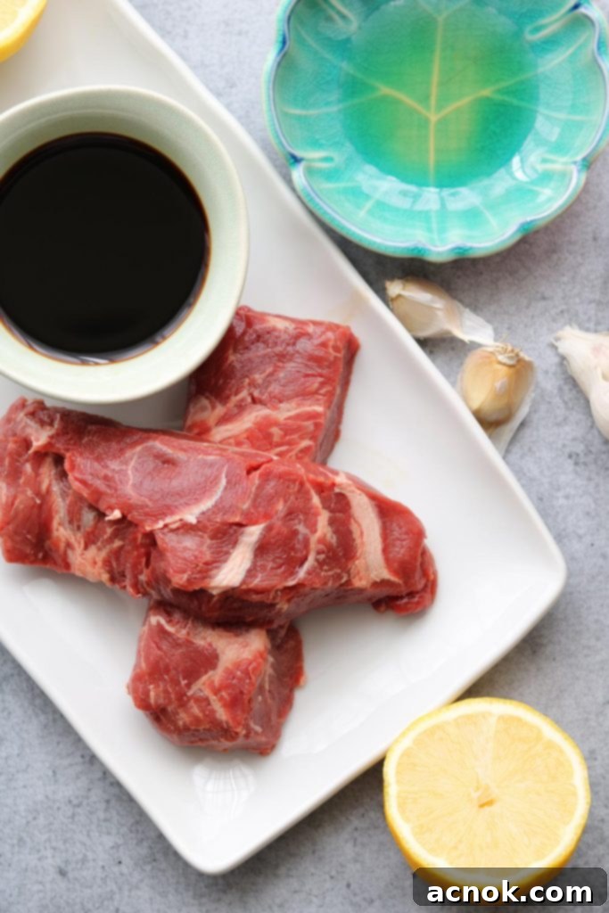 Flat iron steak, low sodium soy sauce, lemon, garlic and toasted sesame oil on a plate, ready for marinade.