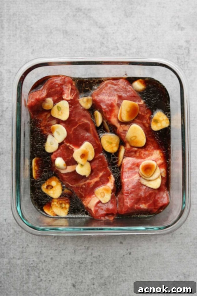 Flat iron steak submerged in lemon soy marinade with garlic slices.