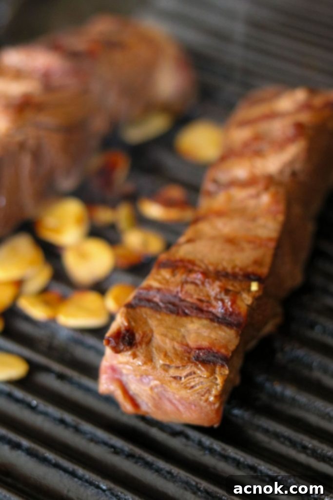 Flat iron steaks cooking on a stovetop grill, with garlic slices charring beautifully.