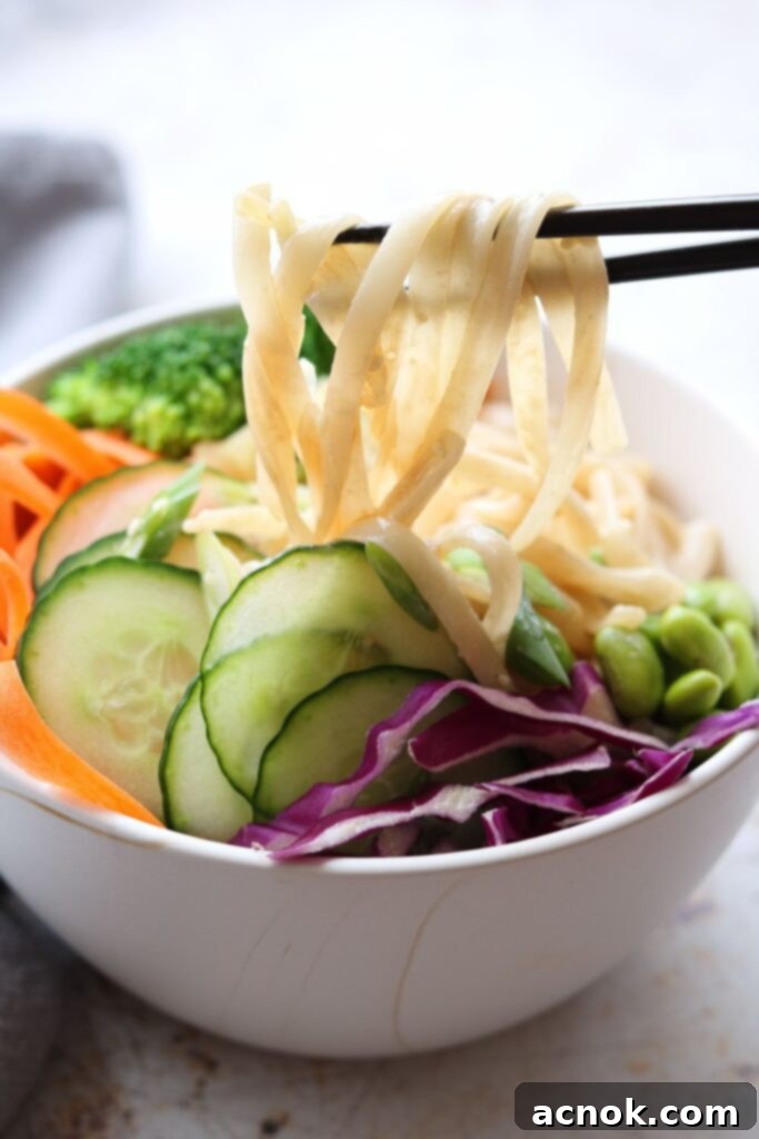 creamy sesame rice noodles in bowl being picked up by chopsticks