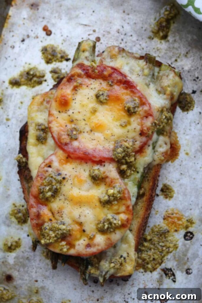 Roasted Asparagus Tomato Pesto Melt on a baking sheet with a drizzle of pesto, ready to be served