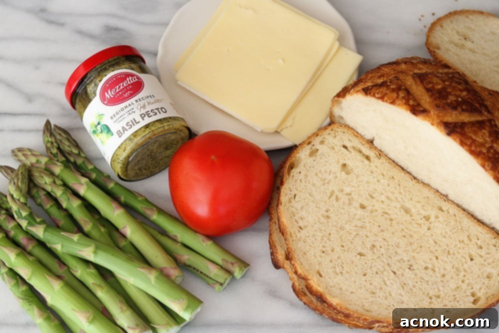 Ingredients for Roasted Asparagus Tomato Pesto Melt laid out on a marble background