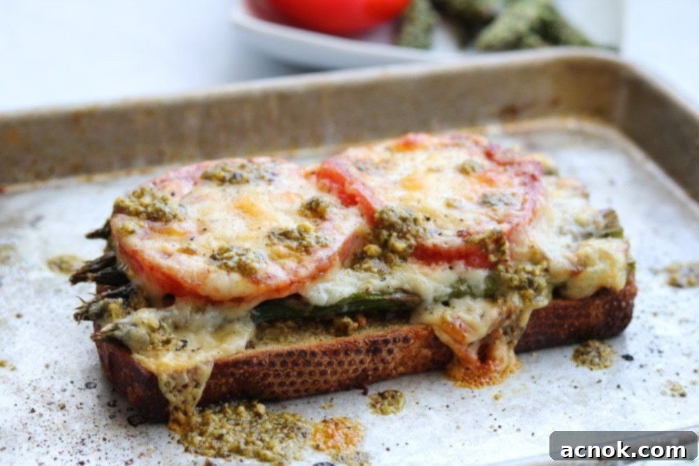A close-up of a Roasted Asparagus Tomato Pesto Melt on a baking sheet, freshly melted with a golden-brown top