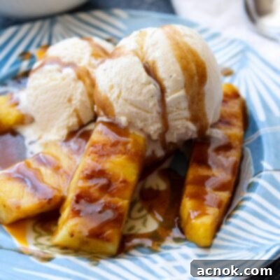 Close-up of grilled pineapple with spiced rum butter sauce and melted vanilla ice cream in a white bowl.