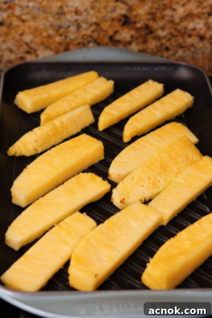 Raw pineapple spears being carefully placed onto a hot, seasoned grill pan.