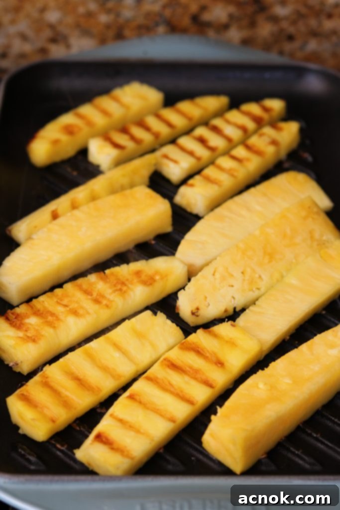 Pineapple spears grilling on a griddle, showing distinct brown grill marks and slight softening.