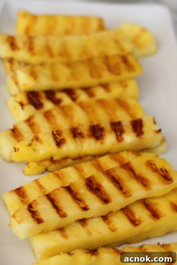 Grilled pineapple spears arranged neatly on a white serving platter, ready for the sauce.