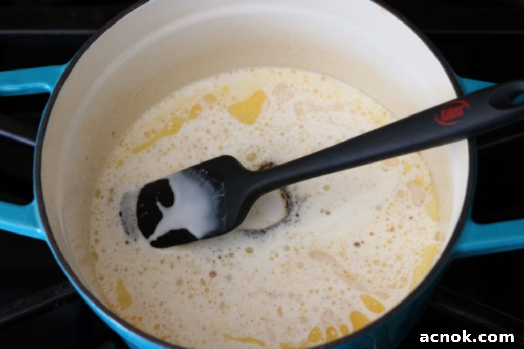 Heavy whipping cream and spiced rum being poured into the melted butter and sugar mixture in the pot.