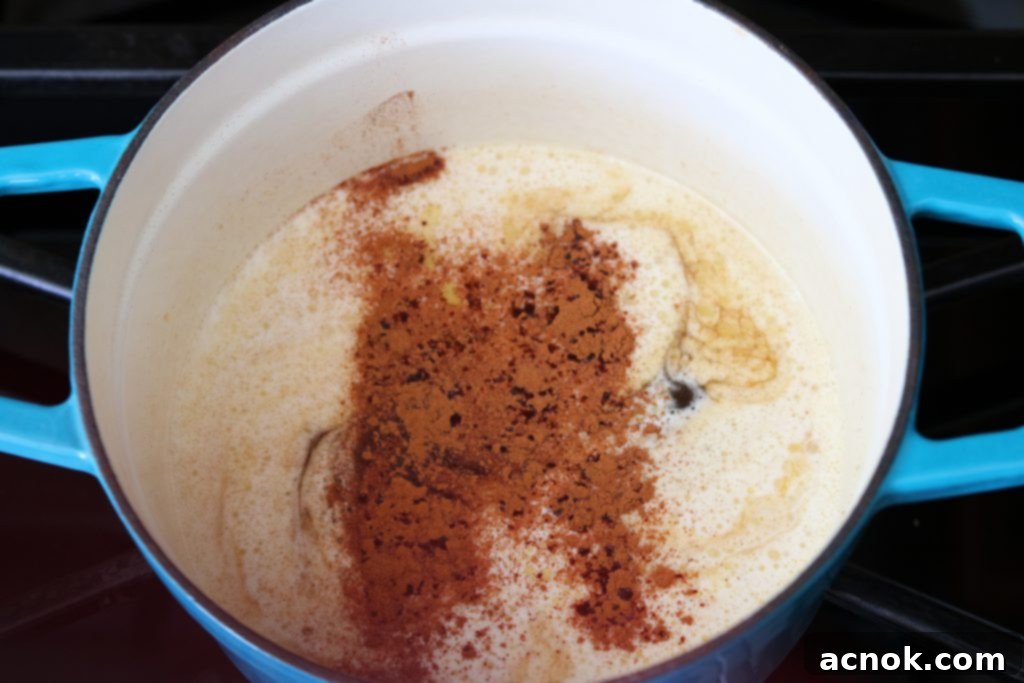 A small spoonful of ground cinnamon being added to the spiced rum butter sauce as it simmers.