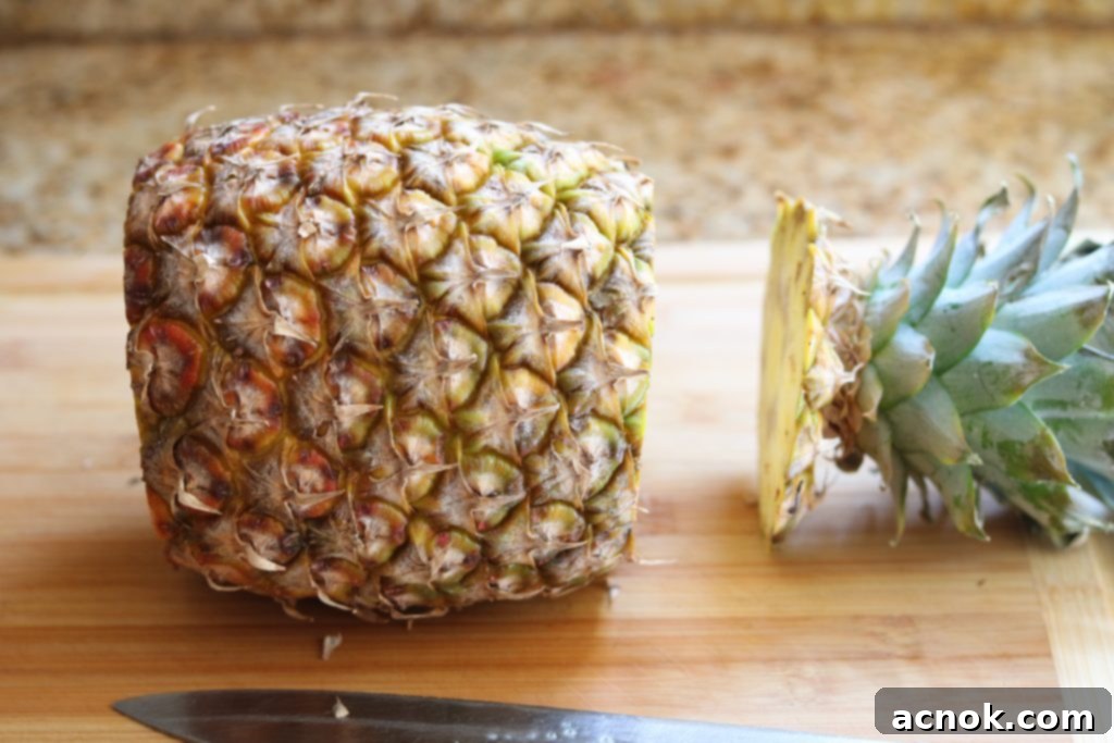Top of pineapple with leafy crown removed, sitting on a cutting board