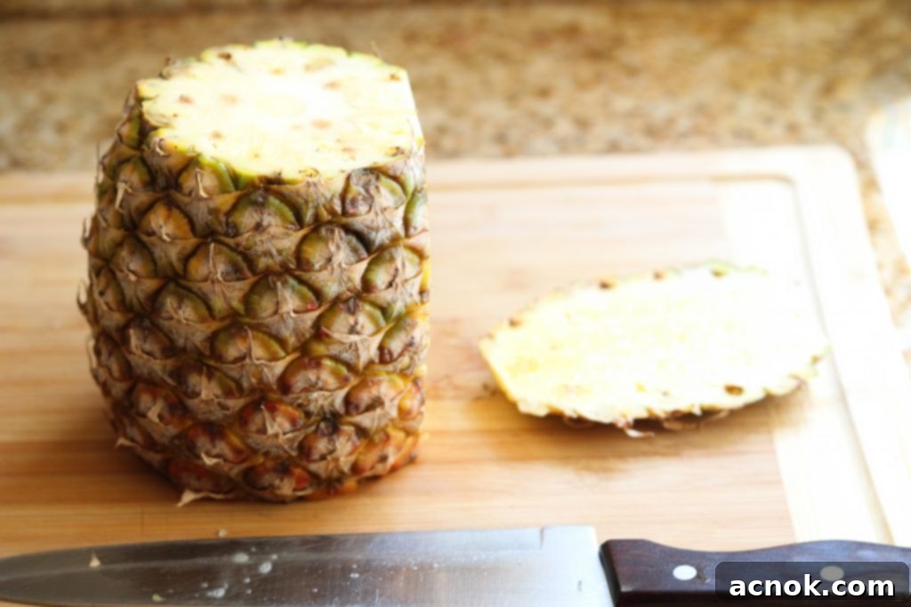 Chef's knife carefully slicing off the skin from the sides of a pineapple