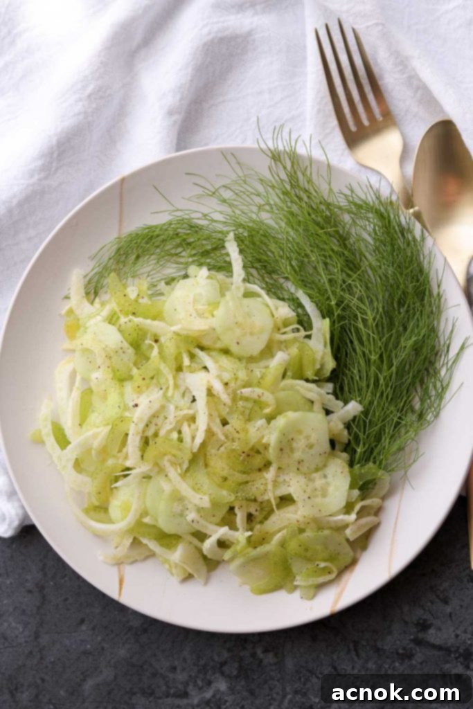 A vibrant bowl of Shaved Fennel, Cucumber, and Celery Salad, glistening with dressing and topped with fresh herbs.