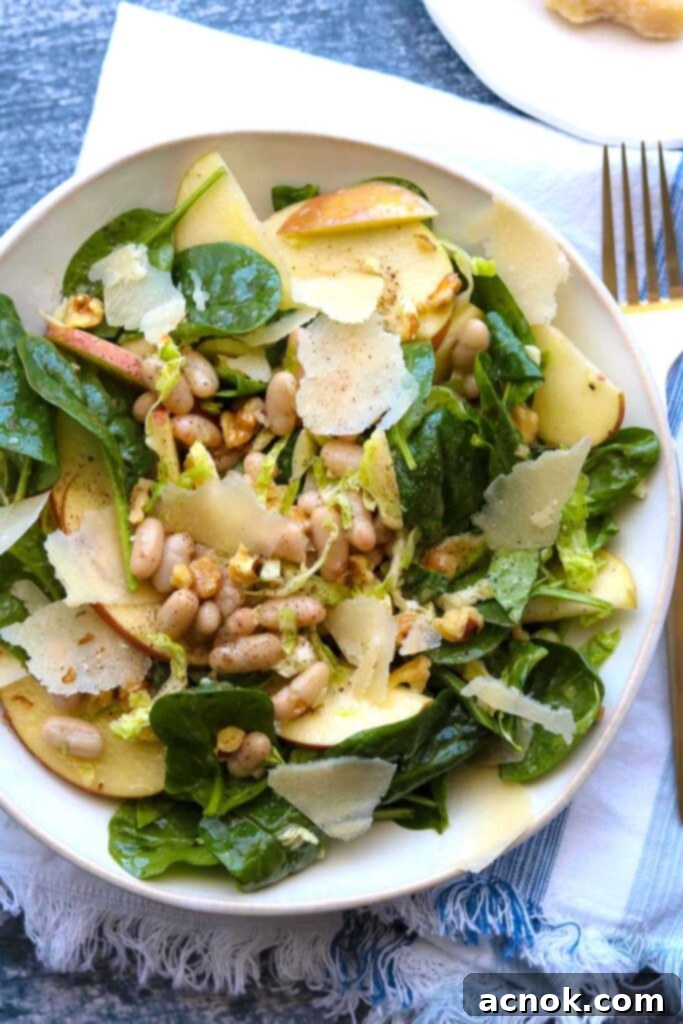 Apple Spinach White Bean Salad on a plate with a napkin and fork, showcasing fresh ingredients.