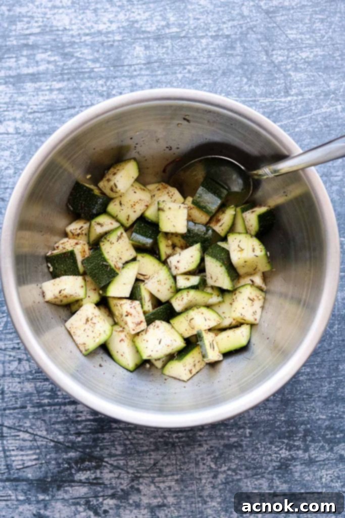 Raw zucchini being tossed vigorously by hand to evenly coat with olive oil and Za'atar blend in a bowl