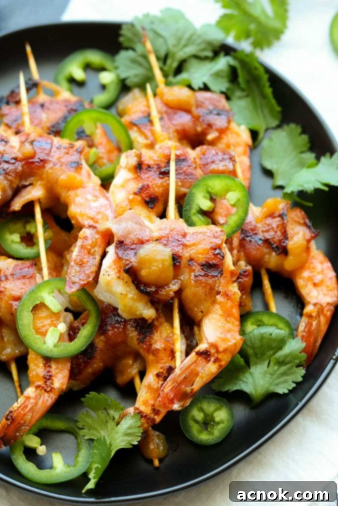 Grilled bacon-wrapped shrimp skewers garnished with fresh jalapeño slices and cilantro, ready to serve.
