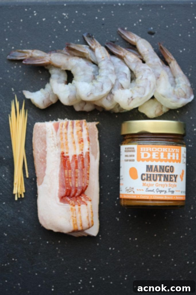 Ingredients for Chutney Glazed Bacon Wrapped Shrimp: raw peeled and deveined jumbo shrimp, bamboo skewers, strips of bacon, and a jar of mango chutney.