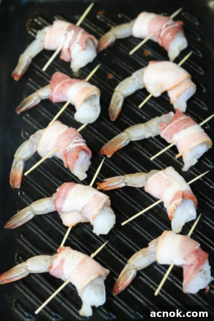 Bacon wrapped shrimp skewers cooking on a preheated stovetop grill pan, showing initial searing.