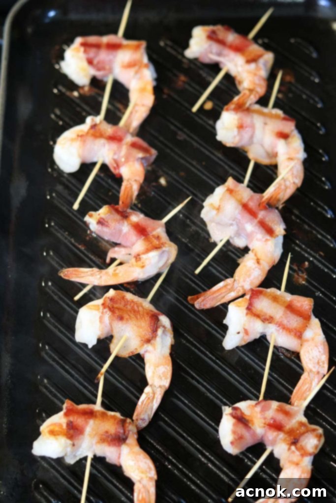 Close-up of bacon wrapped shrimp skewers being turned on the grill, showing browning on one side.