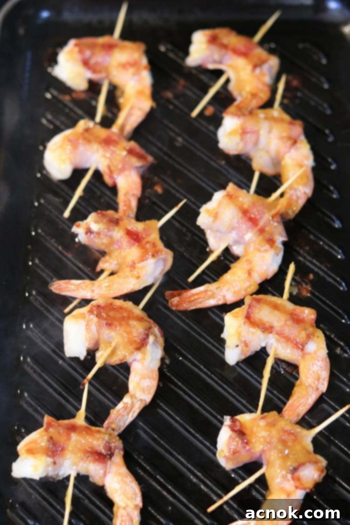 Partially cooked bacon wrapped shrimp skewers on the grill, with mango chutney being brushed on.