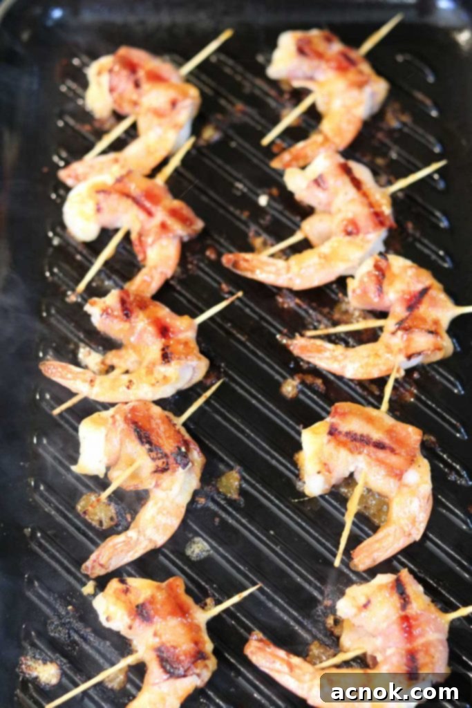 Chutney glazed bacon wrapped shrimp skewers caramelizing on the grill, showing a rich, glossy coating and grill marks.