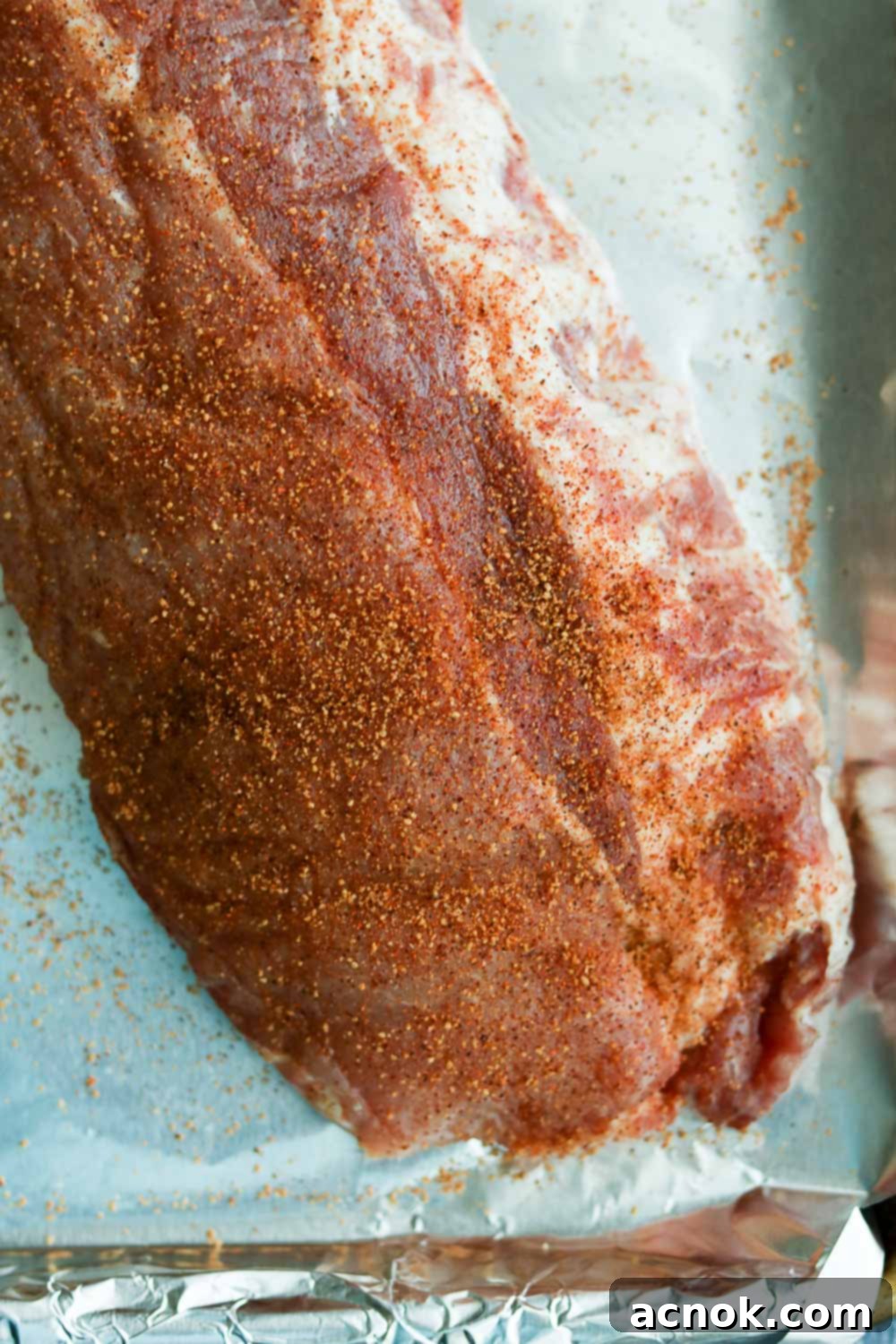 Close up of raw pork ribs generously coated with a dark, savory dry rub, ready for seasoning.