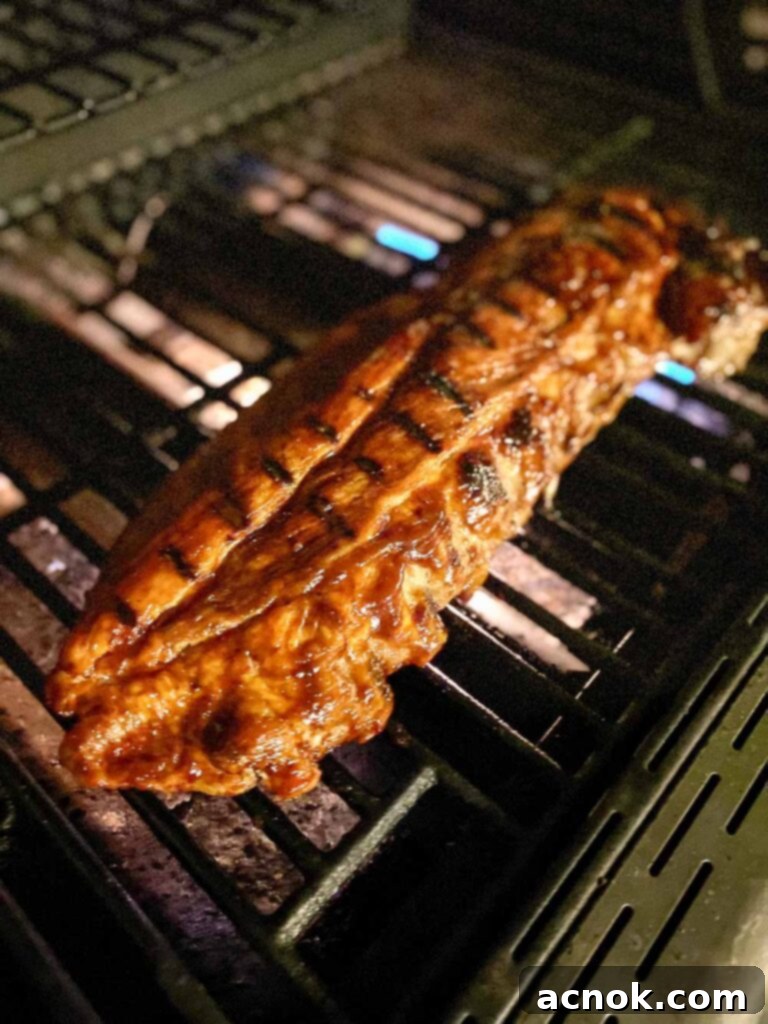 Tender BBQ ribs grilling on an outdoor gas grill, showing beautiful char and ready to be sauced.