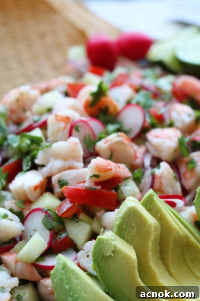 Close-up side view of a perfectly assembled shrimp ceviche style tostada, topped with creamy avocado slices and fresh cilantro.