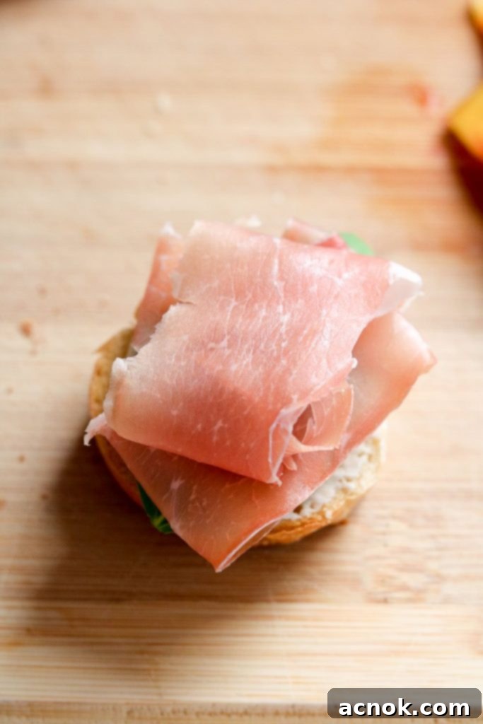 Small slices of prosciutto being added to a crostini
