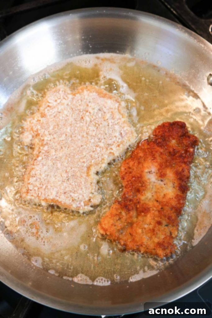 Chicken Schnitzel frying in a cast iron pan, turning golden brown and crispy.