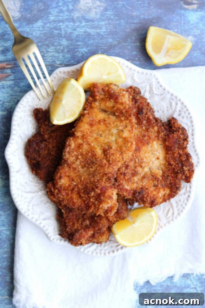 easy chicken schnitzel on white plate with lemon garnish white napkin and fork