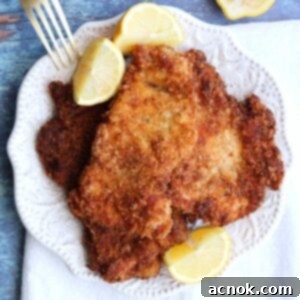 chicken schnitzel square with lemons fork on white plate