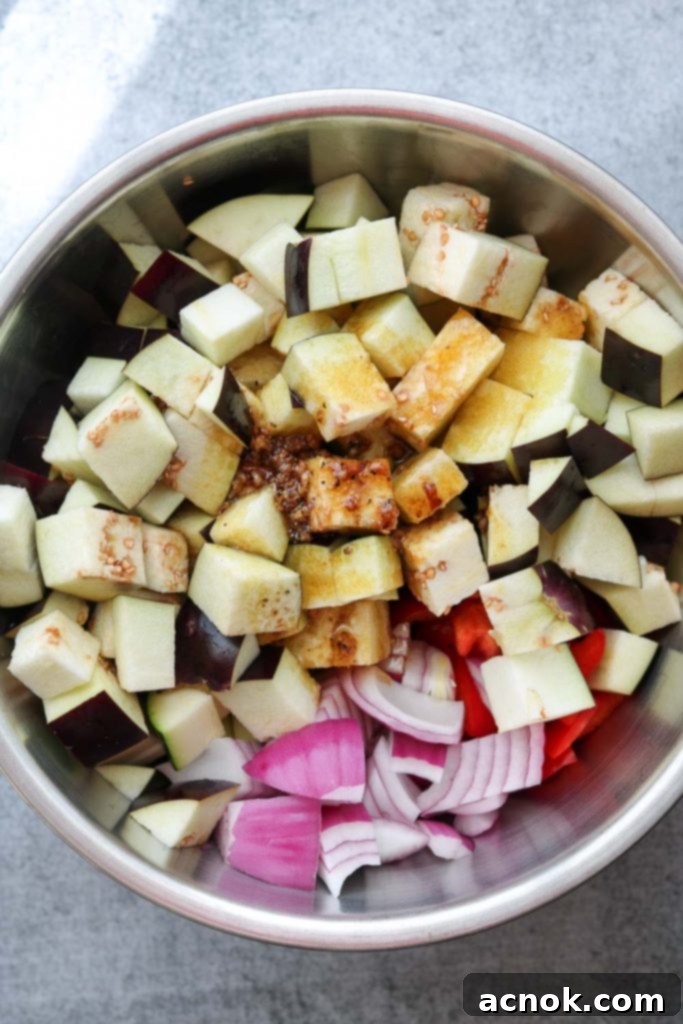 Close-up of cubed vegetables in a bowl, with olive oil, balsamic vinegar, and dried thyme being poured over them.