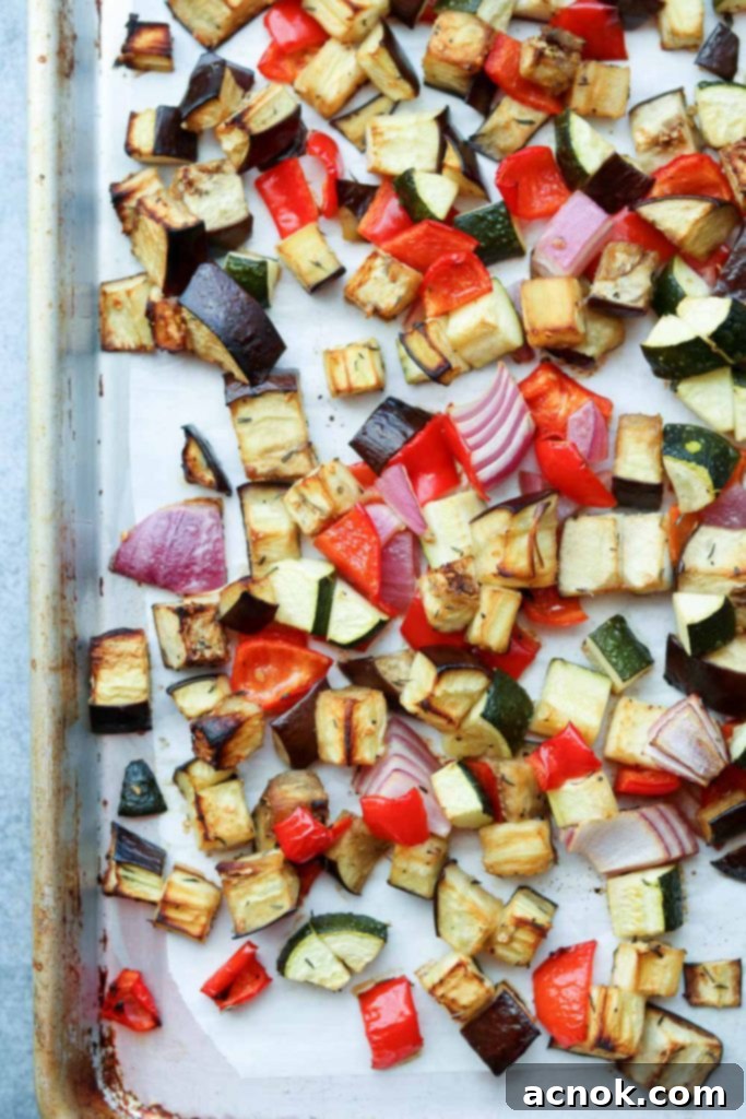 Close-up of roasted vegetables on a baking sheet, showing tender textures and slightly charred edges.